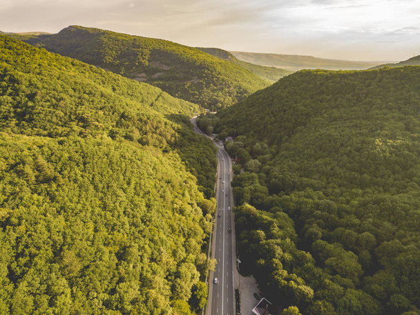 вид з повітря на широке шосе між горами, покритими зеленими лісами б
 - Фото, зображення