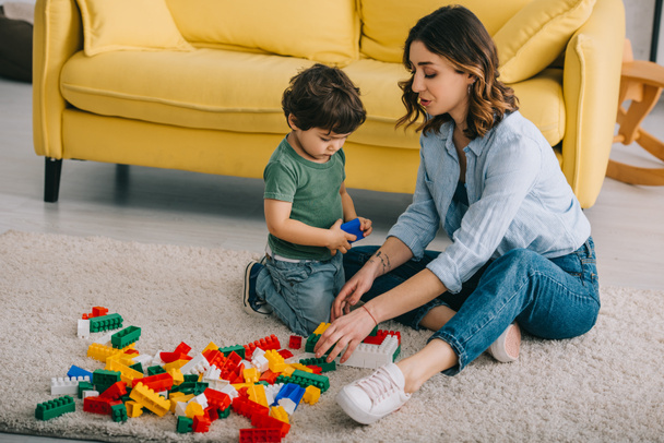 Mother and son playing with lego on carpet in living room - Foto, Bild