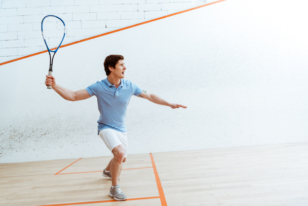Emotional sportsman in blue polo shirt playing squash in four-walled court - Zdjęcie, obraz