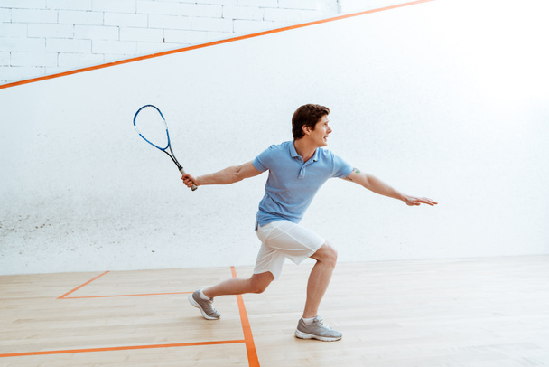 Emotionele sportman in blauwe poloshirt spelen squash in vierwandige Hof - Foto, afbeelding