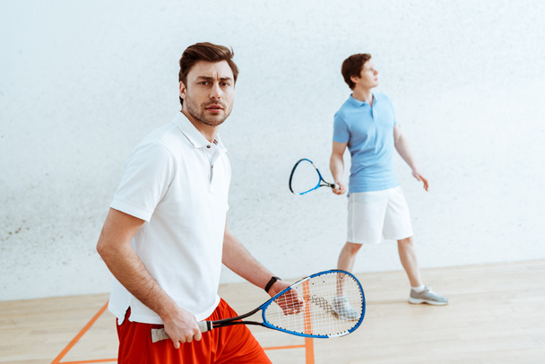 Barbudo jugador de squash con raqueta mirando a la cámara
 - Foto, Imagen