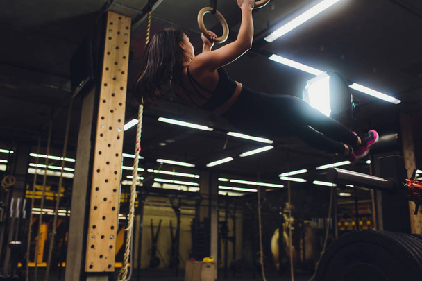 Young athletic sportswoman exercising on gymnastic rings at gym. - Foto, imagen