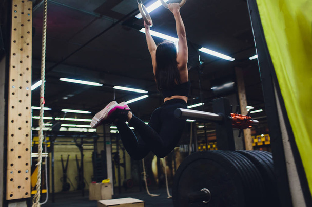 Young athletic sportswoman exercising on gymnastic rings at gym. - Foto, Imagen