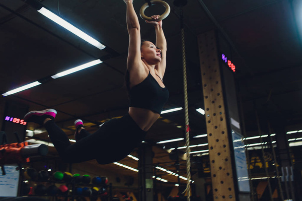 Young athletic sportswoman exercising on gymnastic rings at gym. - Fotó, kép