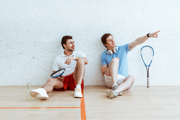 Squash player seduto sul pavimento con un amico e che punta con il dito
 - Foto, immagini