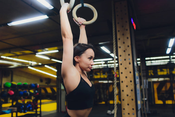 Young athletic sportswoman exercising on gymnastic rings at gym. - Фото, зображення