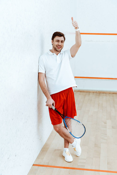 Вид в полный рост игрока в сквош в красных шортах, держащего рейнджеры и показывающего большой палец вверх
 - Фото, изображение