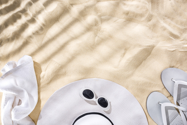 vista superior de toalla blanca, gafas de sol retro, chanclas y sombrero floppy con cinta negra en la arena con sombras y espacio de copia
 - Foto, imagen