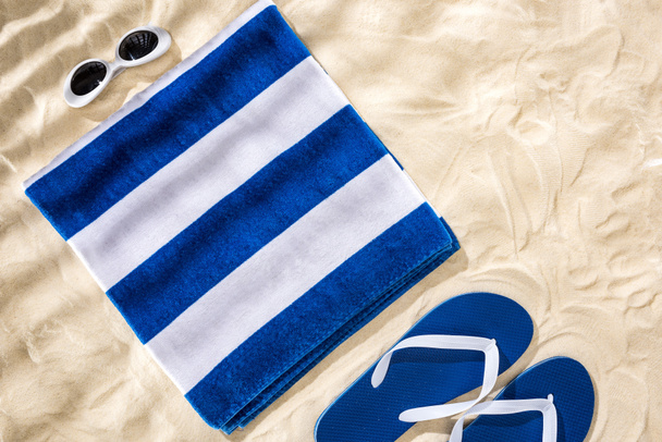 Widok z góry biały niebieski paski składany ręcznik, okulary retro i klapki na piasku  - Zdjęcie, obraz