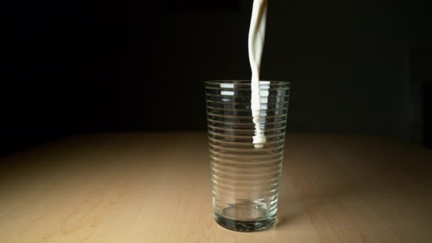 süper yavaş hareket: Lezzetli soğuk süt ahşap masa üzerinde boş bardağa dökülür. Beyaz sıvı akıyor ve boş camın etrafına sıçrıyor. Kahvaltıda cama dökülen lezzetli organik keçi sütü. - Video, Çekim