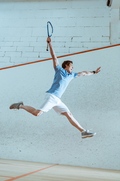 Full length view of excited sportsman in blue polo shirt jumping while playing squash - Foto, immagini