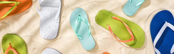 panoramic shot of scattered white, turquoise, green and blue flip flops on sand - Photo, Image