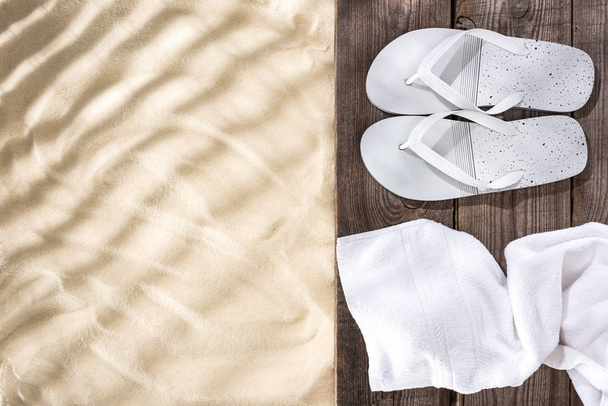 Top view of white flip flops and towel on wooden brown board and sand with copy space - Foto, imagen