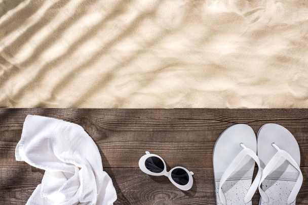 top view of sand with copy space and white towel, retro sunglasses and flip flops on wooden brown board  - Photo, Image