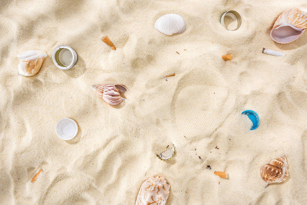 貝殻、ボトルキャップ、散乱タバコの吸殻、砂の上のペットボトルキャップのトップビュー - 写真・画像