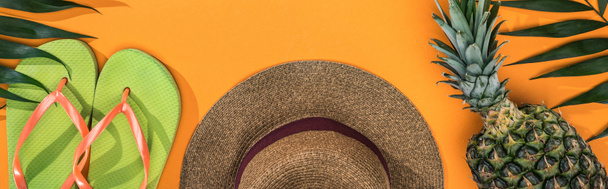 panoramic shot of pineapple, tropical leaves, green flip flops and brown straw hat on orange background - Photo, Image