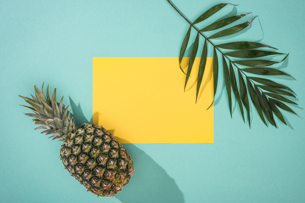 vista superior de piña, hoja tropical y tarjeta amarilla con espacio para copiar sobre fondo turquesa
 - Foto, Imagen