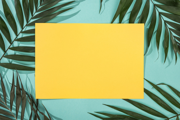 Draufsicht auf tropische Blätter und leere gelbe Karte auf türkisfarbenem Hintergrund - Foto, Bild