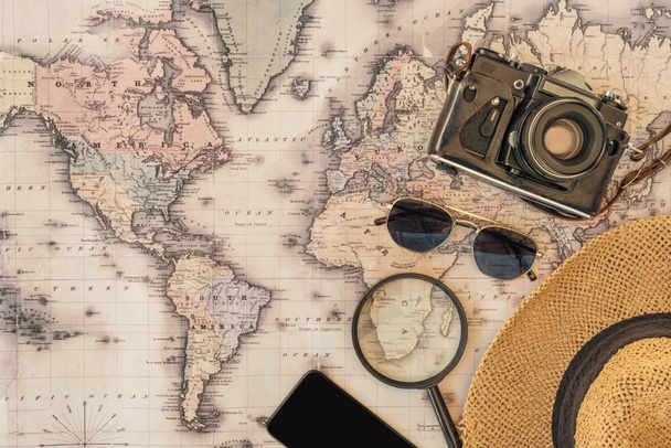 Vista superior de chapéu de palha, óculos de sol, câmera de filme, lupa e smartphone com tela em branco no mapa do mundo
 - Foto, Imagem