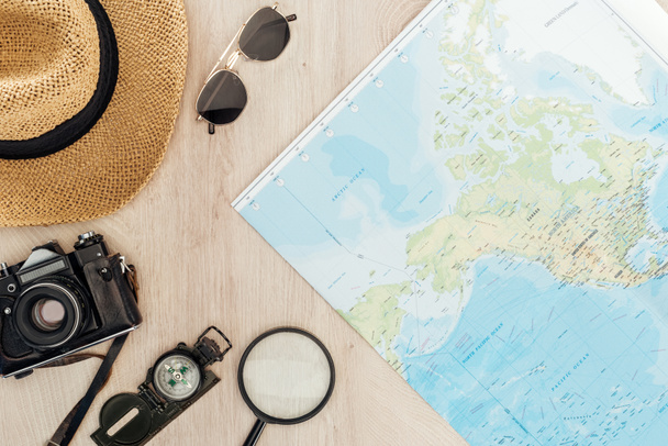 Вид сверху солнцезащитных очков, соломенной шляпы, компаса, лупы, кинокамеры и карты мира на деревянной поверхности
 - Фото, изображение