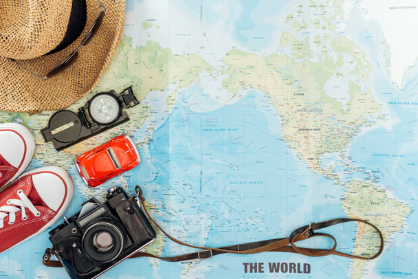 Vue de dessus des chaussures en gomme, chapeau de paille, caméra de film, lunettes de soleil. jouet voiture et boussole sur la carte du monde
 - Photo, image