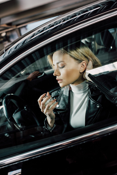 attractive driver sitting in car and holding bottle of perfume  - Foto, afbeelding