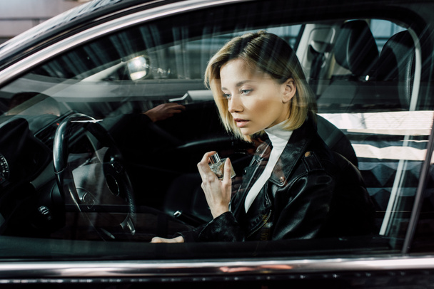 attractive blonde woman holding perfume bottle in car  - Foto, afbeelding