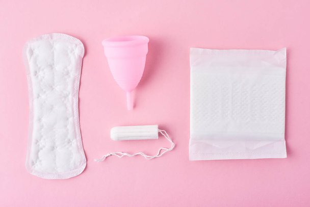 Sanitaire pad, menstruele beker en tampon op een roze achtergrond, bovenaanzicht - Foto, afbeelding