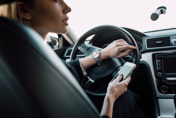 cropped view of blonde woman sitting in car and holding smartphone  - Fotó, kép