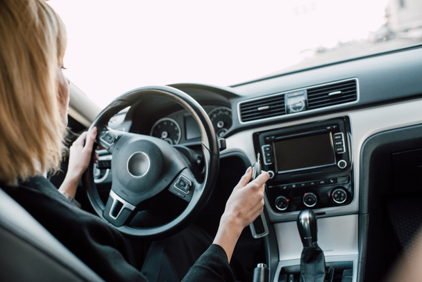 oříznutý pohled blonďaté ženy přidržením klíče a volantu při sezení v autě  - Fotografie, Obrázek