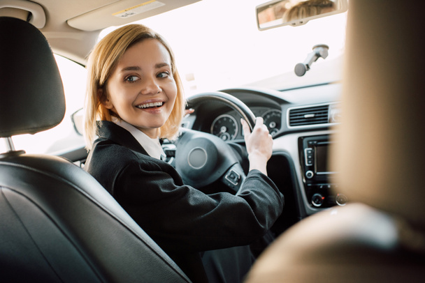 χαρούμενη ξανθιά γυναίκα κρατώντας το τιμόνι ενώ κάθεται στο αυτοκίνητο  - Φωτογραφία, εικόνα