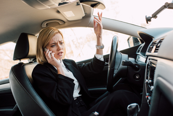 upset blonde young woman talking smartphone while sitting in car  - Photo, Image