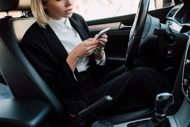 車の中に座っている間、スマートフォンを使用してブロンドの若い女性のトリミングビュー  - 写真・画像