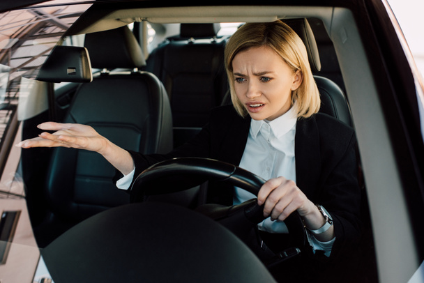 upset blonde girl holding steering wheel while gesturing and driving car  - Foto, imagen