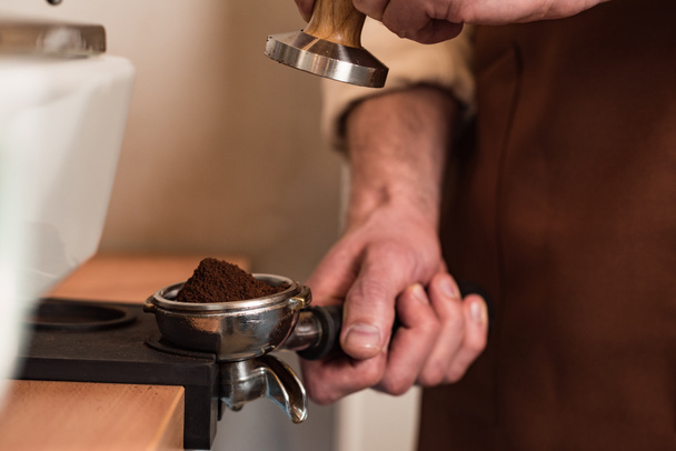 Περικομμένη θέα του μπάρμαν σε καφέ ποδιά προετοιμασία καφέ - Φωτογραφία, εικόνα