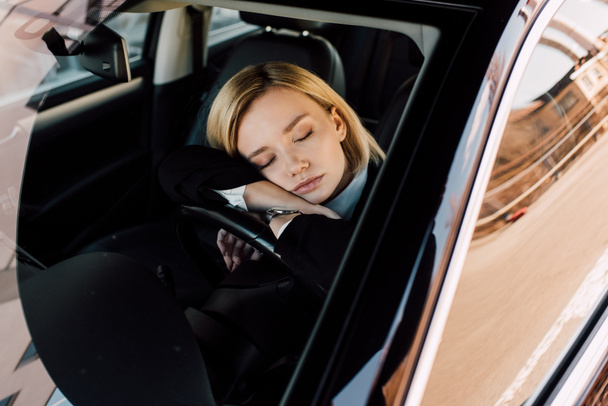tired blonde young woman sleeping in modern automobile near steering wheel  - Zdjęcie, obraz