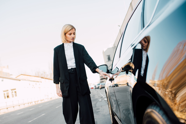beautiful blonde woman standing near black car in parking  - Photo, Image