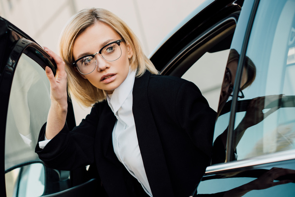 beautiful blonde young woman in glasses near black automobile  - Fotoğraf, Görsel