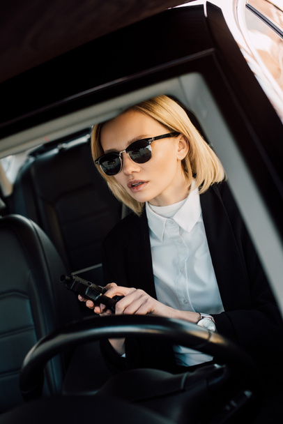 atractiva chica rubia en gafas de sol sosteniendo pistola en el coche
  - Foto, Imagen