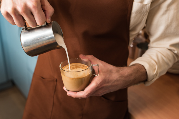 Обрезанный вид на баристу, наливающую молоко в кофе
 - Фото, изображение