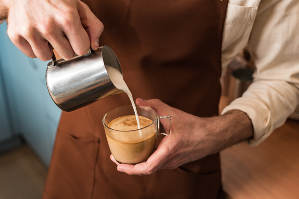 Bijgesneden beeld van Barista gieten melk in koffie - Foto, afbeelding