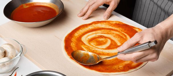 Chef-kok verspreiden tomatenpuree op pizza base - Foto, afbeelding