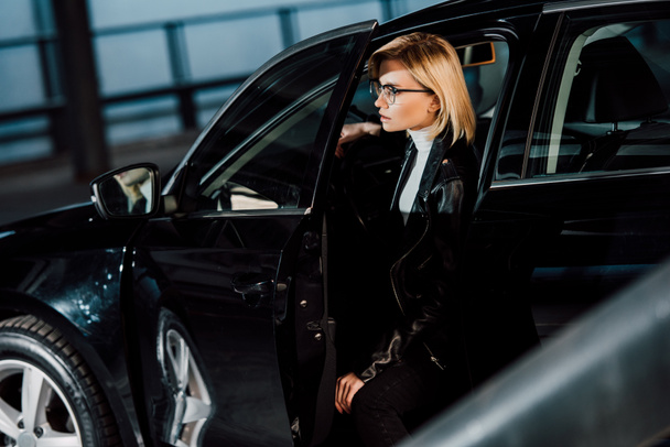 jolie jeune femme blonde dans des lunettes assis en voiture noire
  - Photo, image