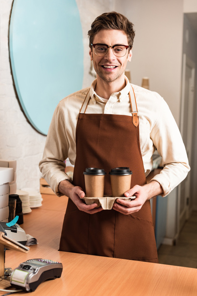 Smiling barista in glasses holding take-out cup carrier with coffee - Photo, Image