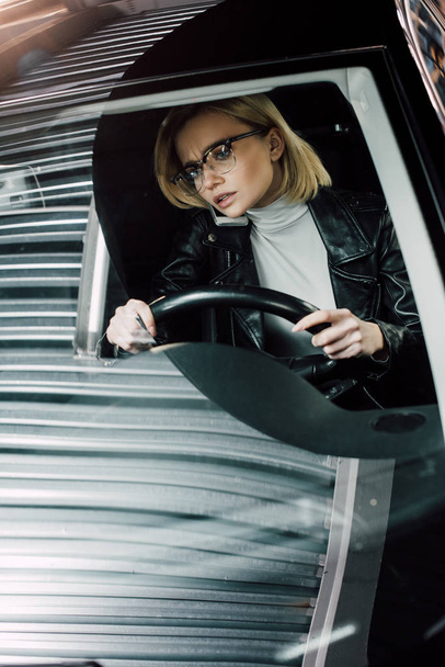 блондинка приваблива дівчина говорить смартфон, тримаючи кермо в машині
  - Фото, зображення