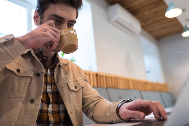 Фрилансер пьет кофе и пользуется ноутбуком в кафе
 - Фото, изображение