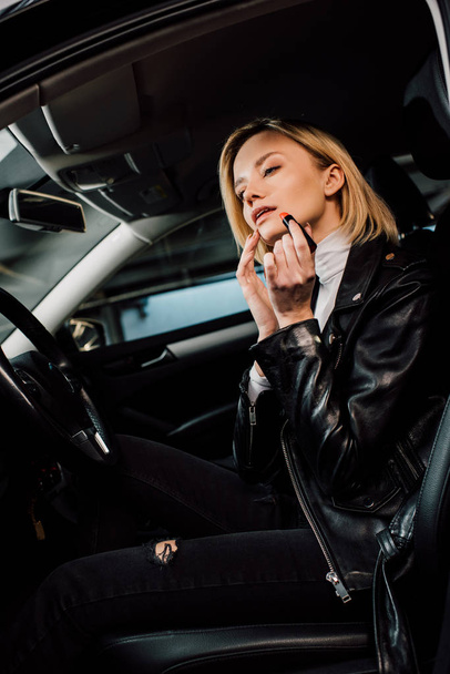 Mały kąt widzenia atrakcyjne blonde girl stosowania szminki w samochodzie  - Zdjęcie, obraz