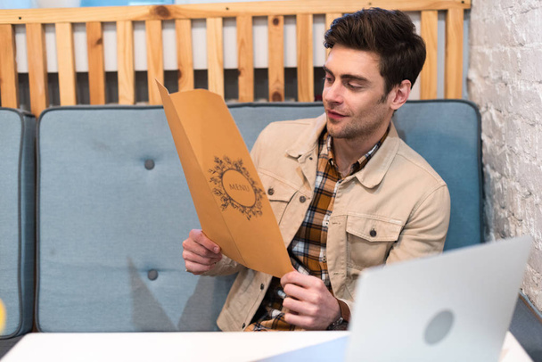 Freelancer in jacket with laptop reading menu in cafe - Zdjęcie, obraz