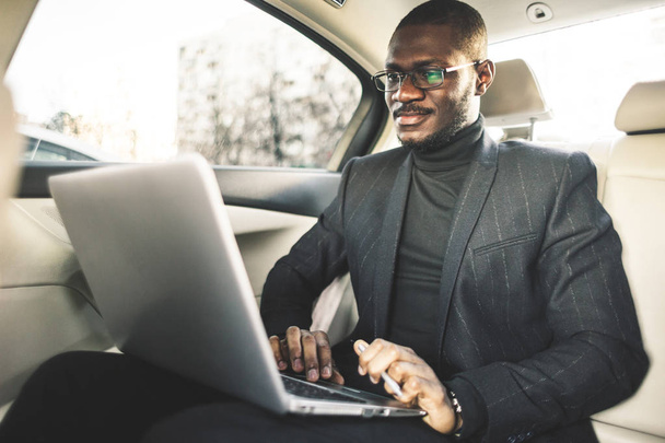 Man in a business suit write on laptop in the salon of an expensive car with leather interior. - Fotoğraf, Görsel
