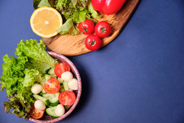 frisches Gemüse und eine Schüssel Salat mit Mozzarella auf blauem Hintergrund. Caprese-Salat. Salat, Kirschtomaten, Mozzarella,  - Foto, Bild